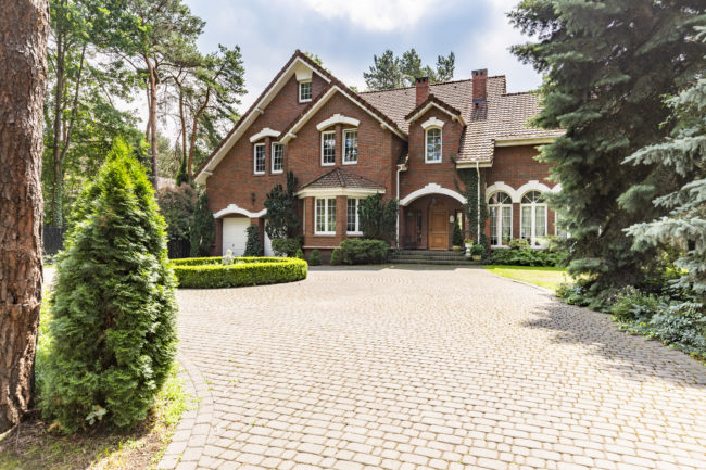 Large cobbled driveway in front of an impressive red brick English design mansion surrounded by old trees